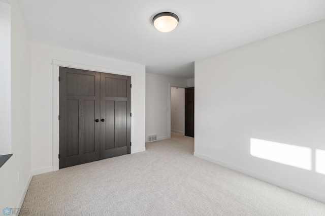 unfurnished bedroom featuring a closet, light colored carpet, baseboards, and visible vents