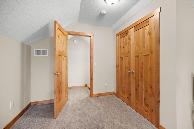 corridor featuring lofted ceiling, light carpet, and a textured ceiling