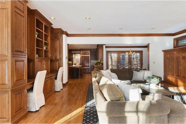 living room featuring crown molding, built in desk, wood-type flooring, and a chandelier