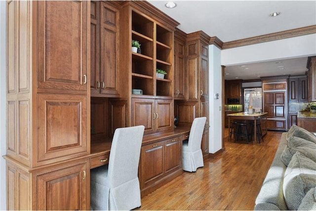 office space featuring wood-type flooring, built in desk, and crown molding