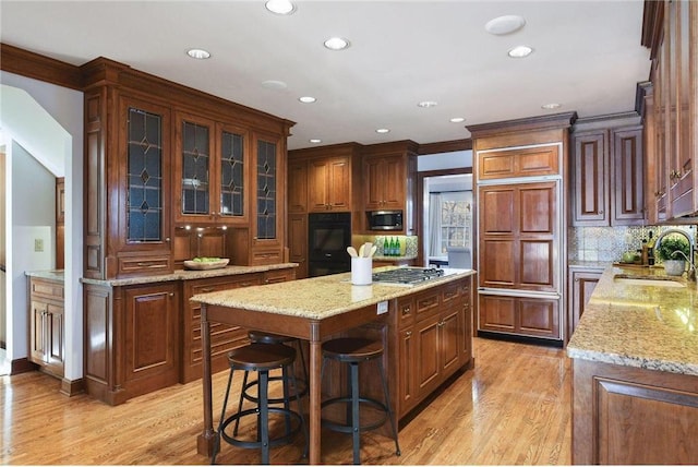 kitchen with appliances with stainless steel finishes, sink, a center island, light stone counters, and light hardwood / wood-style flooring