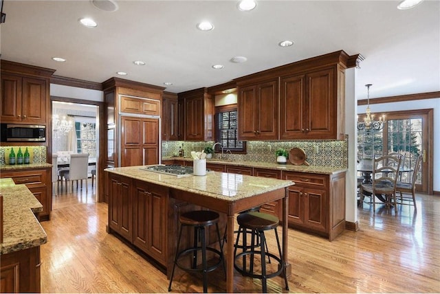 kitchen featuring light hardwood / wood-style flooring, hanging light fixtures, a kitchen island, stainless steel appliances, and backsplash