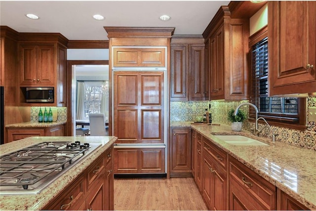 kitchen featuring stainless steel appliances, sink, light stone counters, and light hardwood / wood-style floors