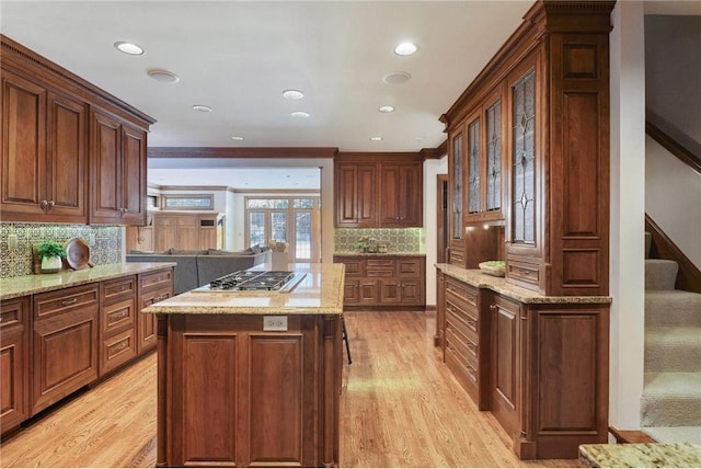 kitchen featuring stainless steel gas stovetop, a kitchen island, light stone counters, and light hardwood / wood-style flooring