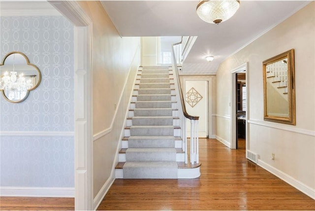 staircase with visible vents, an inviting chandelier, wood finished floors, and wallpapered walls