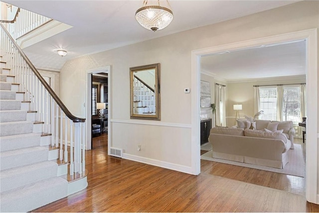 foyer entrance with baseboards, wood finished floors, visible vents, ornamental molding, and stairway
