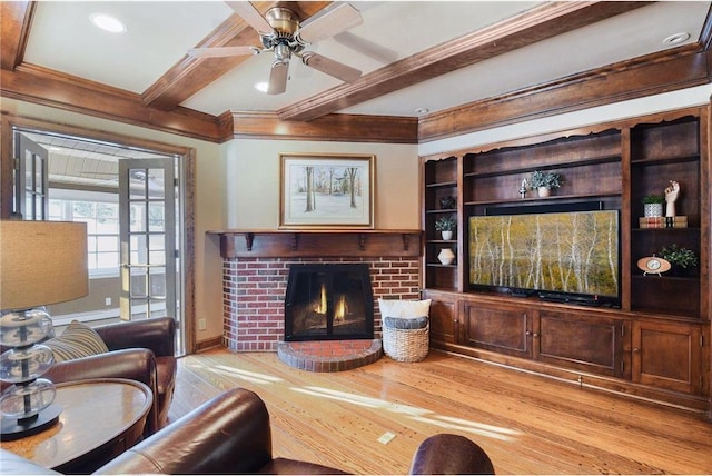 living room with beam ceiling, a brick fireplace, light wood-style flooring, a ceiling fan, and ornamental molding