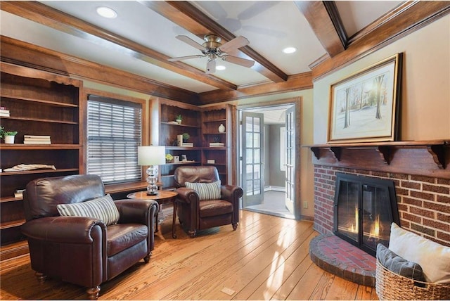 sitting room with crown molding, a brick fireplace, a healthy amount of sunlight, light wood-style floors, and a ceiling fan