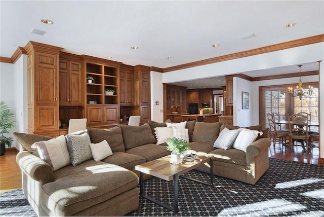 living room with crown molding, visible vents, wood finished floors, and a chandelier