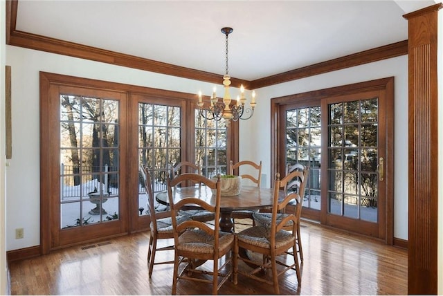 dining space featuring a chandelier, baseboards, wood finished floors, visible vents, and ornamental molding