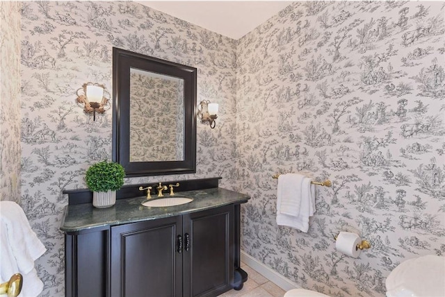 half bathroom with vanity, toilet, tile patterned floors, baseboards, and wallpapered walls