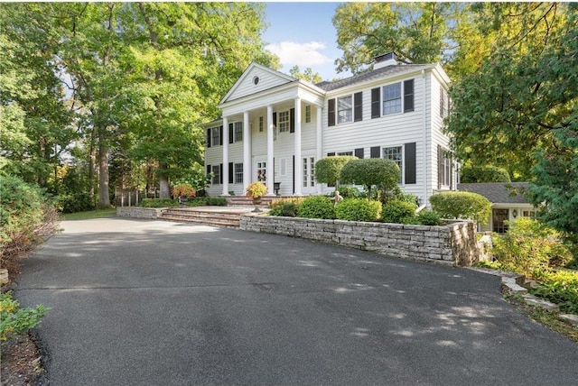 neoclassical / greek revival house featuring a porch, driveway, and a chimney