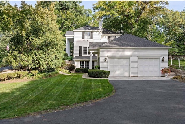 view of front of house featuring an attached garage, a chimney, driveway, and a front lawn