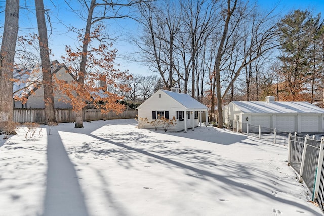 snow covered house featuring fence, a detached garage, an outdoor structure, and a chimney