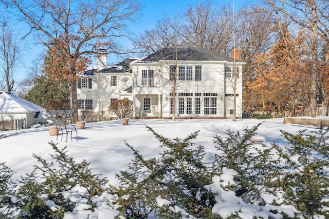 snow covered back of property featuring a chimney