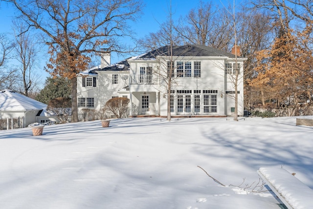 snow covered rear of property featuring a chimney