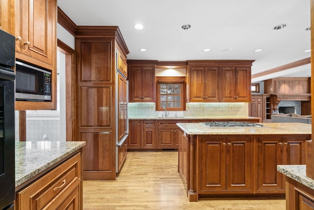 kitchen with tasteful backsplash, light stone countertops, a sink, light wood finished floors, and stainless steel appliances