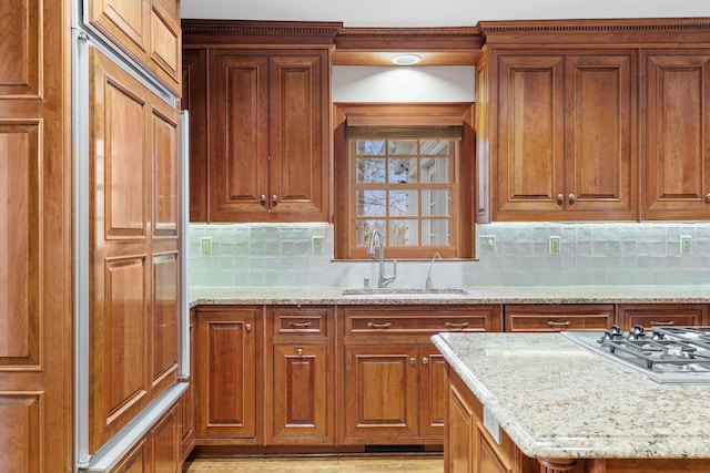 kitchen with light stone counters, a sink, brown cabinetry, and tasteful backsplash