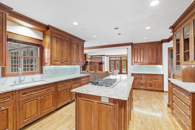 kitchen featuring tasteful backsplash, brown cabinets, a sink, light stone counters, and light wood-style floors