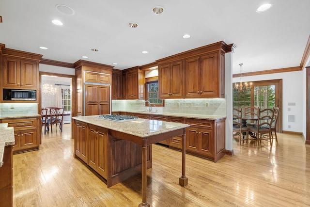 kitchen featuring crown molding, built in appliances, a sink, light wood-style flooring, and a notable chandelier