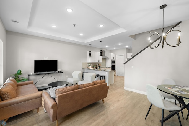 living room with a chandelier, a raised ceiling, sink, and light wood-type flooring