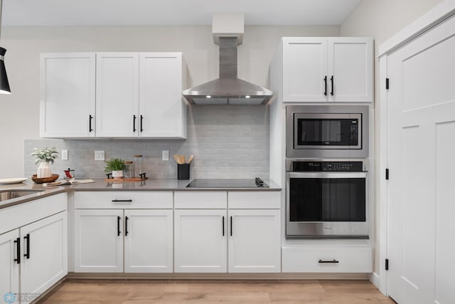 5861 41st St S, Fargo, ND 58104 - kitchen featuring stainless steel appliances, wall chimney range hood, white cabinets, tasteful backsplash, and light wood-type flooring