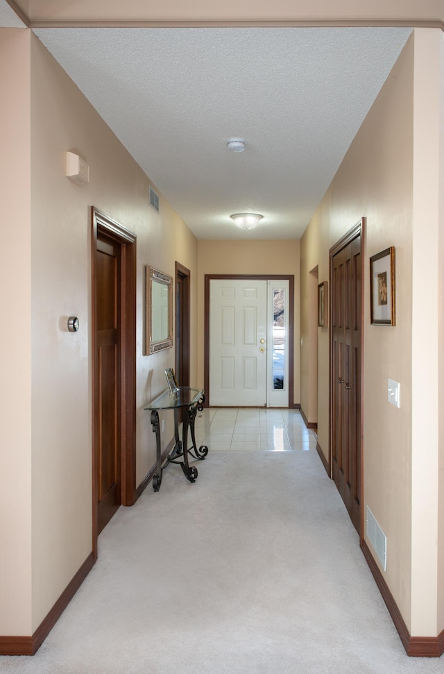 hall featuring a textured ceiling, baseboards, visible vents, and light carpet