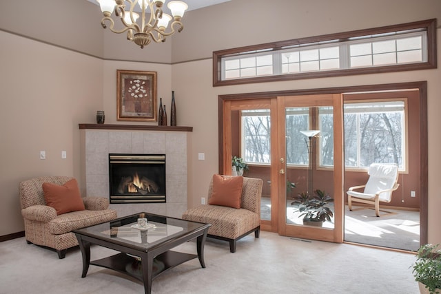 living area with light carpet, a notable chandelier, a tiled fireplace, and baseboards