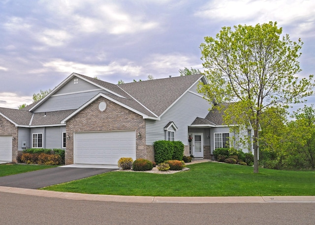 view of front of property featuring driveway, roof with shingles, a front yard, a garage, and brick siding