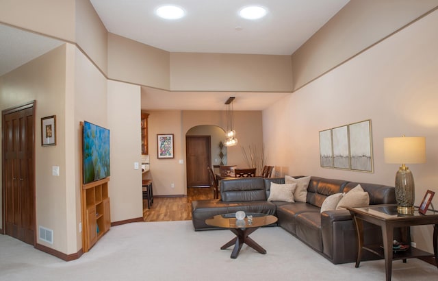 living room featuring light colored carpet, visible vents, arched walkways, and baseboards