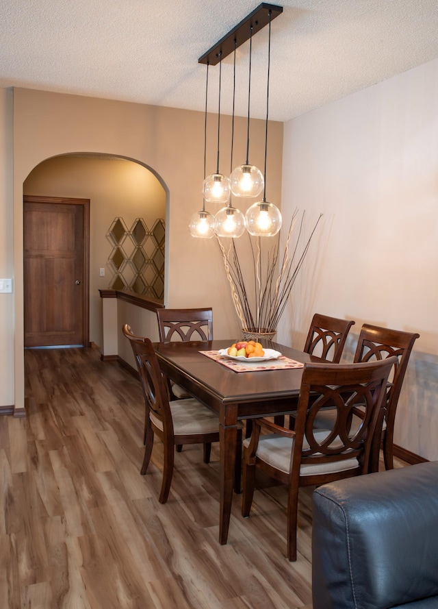 dining area featuring arched walkways, a textured ceiling, baseboards, and wood finished floors