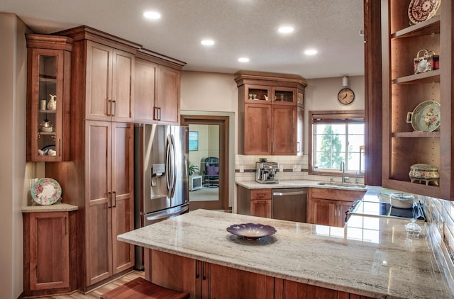 kitchen with a peninsula, a sink, decorative backsplash, glass insert cabinets, and appliances with stainless steel finishes