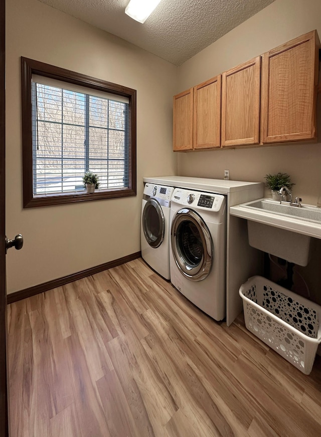 washroom featuring baseboards, light wood-style flooring, cabinet space, a textured ceiling, and separate washer and dryer