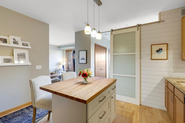 kitchen featuring pendant lighting, butcher block countertops, a center island, a barn door, and light wood-type flooring