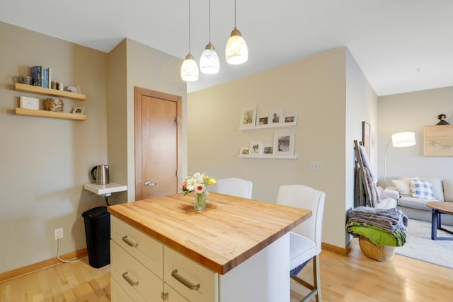 kitchen with a kitchen island, butcher block countertops, a breakfast bar area, hanging light fixtures, and light hardwood / wood-style floors