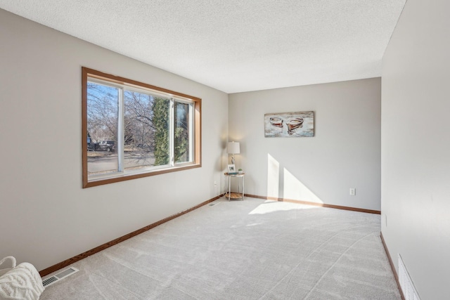 empty room featuring light carpet, baseboards, visible vents, and a textured ceiling