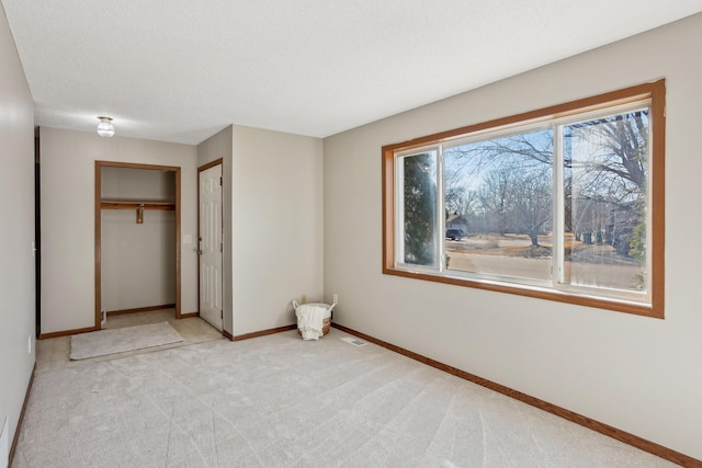 unfurnished bedroom with a closet, light colored carpet, a textured ceiling, and baseboards