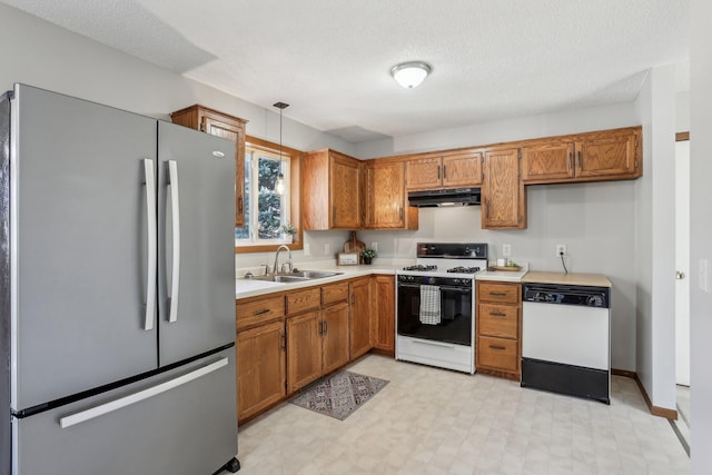 kitchen with white appliances, under cabinet range hood, brown cabinetry, and a sink