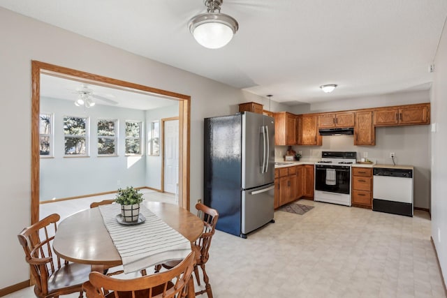 kitchen featuring light countertops, brown cabinetry, white appliances, under cabinet range hood, and baseboards