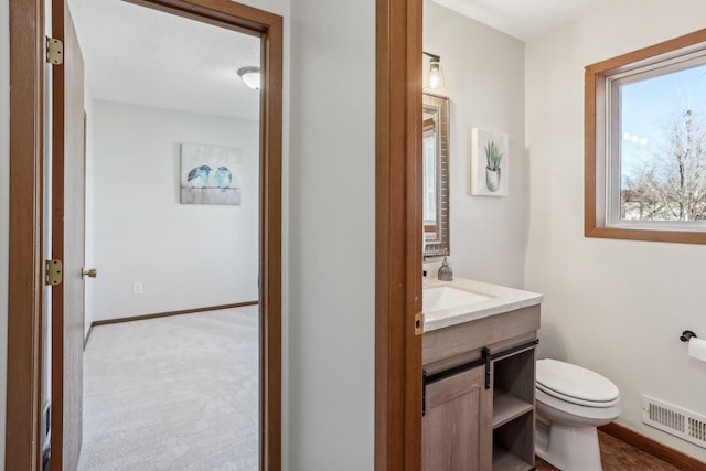 half bathroom with toilet, vanity, visible vents, and baseboards