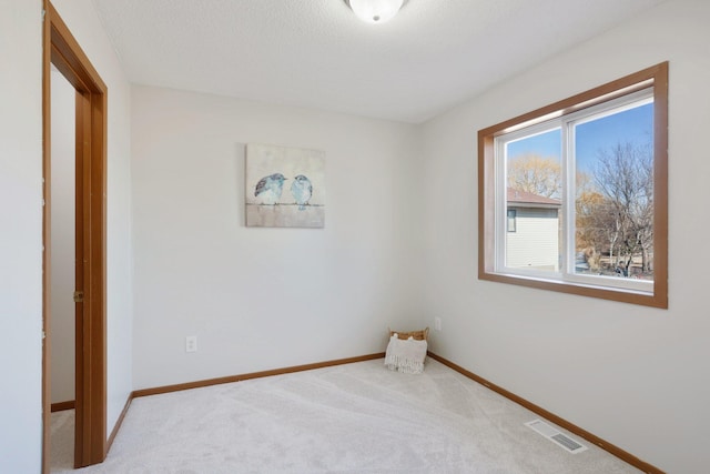 carpeted empty room featuring visible vents, a textured ceiling, and baseboards