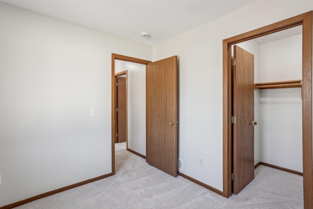 unfurnished bedroom with light carpet, a closet, baseboards, and a textured ceiling