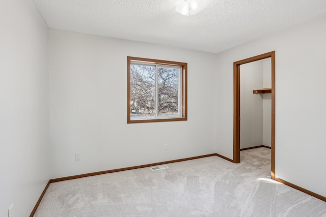 unfurnished room with a textured ceiling, carpet floors, visible vents, and baseboards