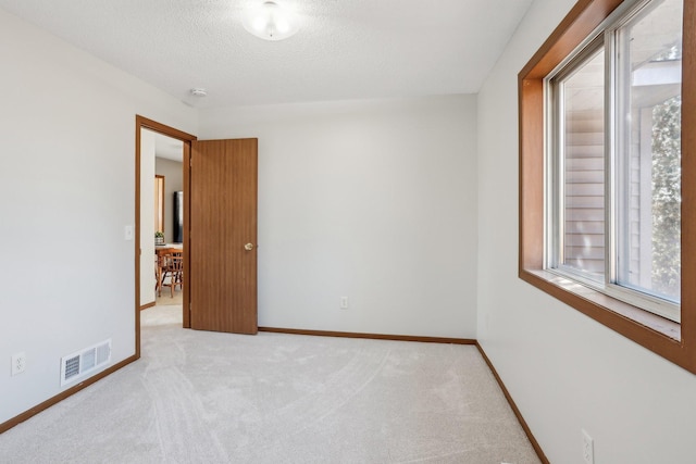 carpeted spare room featuring visible vents, a textured ceiling, and baseboards