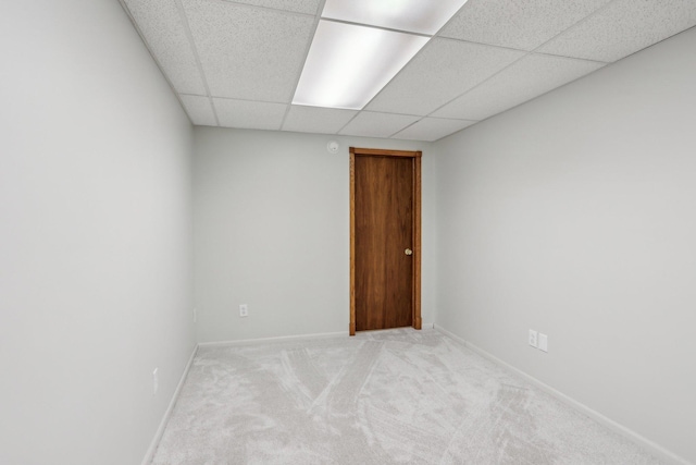 empty room with baseboards, light colored carpet, and a drop ceiling