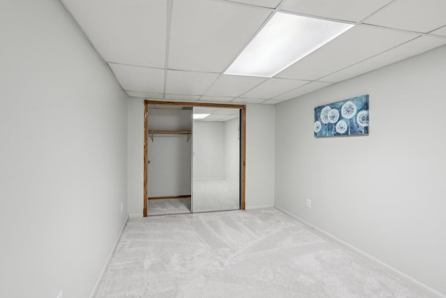 unfurnished bedroom featuring carpet, a closet, a paneled ceiling, and baseboards