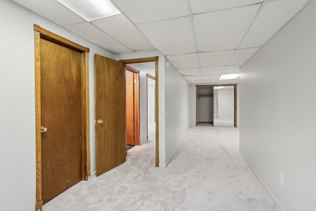 hall with a paneled ceiling, carpet flooring, and baseboards