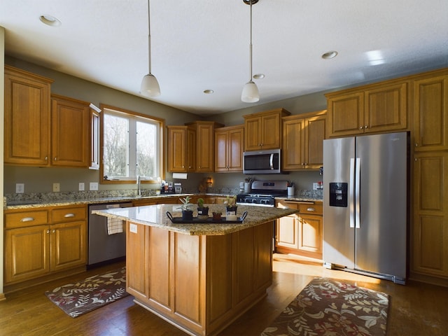 kitchen featuring light stone counters, stainless steel appliances, a kitchen island, hanging light fixtures, and brown cabinets