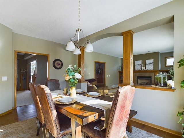 dining room with baseboards, decorative columns, a tiled fireplace, and wood finished floors