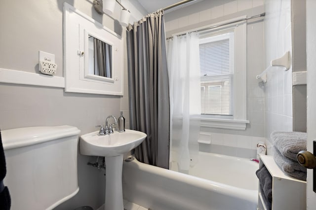 bathroom with toilet, shower / bath combo with shower curtain, and tile walls